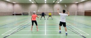 Een badmintonspeler halverwege een bovenhandse slag op de baan