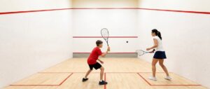 Een jonge speler met squashbril in de klaarstand op een squashbaan