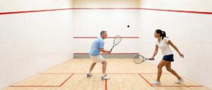 Twee spelers in een rally op een squashbaan, de bal in de lucht voor de voormuur